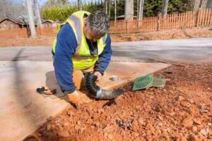 Worker installing a drainage pipe to fix water runoff issues near a concrete driveway in Brunswick OH.
